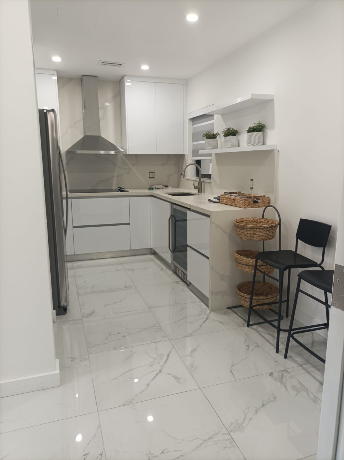 A modern kitchen featuring white cabinets and white marble floors with grey veining.