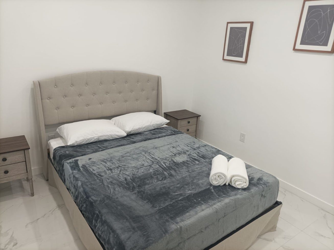 A finished bedroom with a tufted headboard, freshly painted white walls and marble tiled floors.