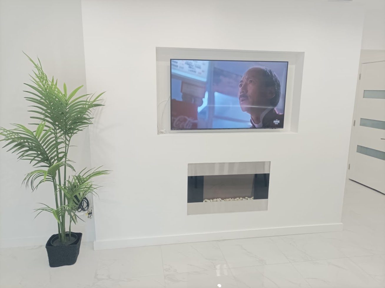 A flat screen television and electric fireplace set into a smooth white wall.