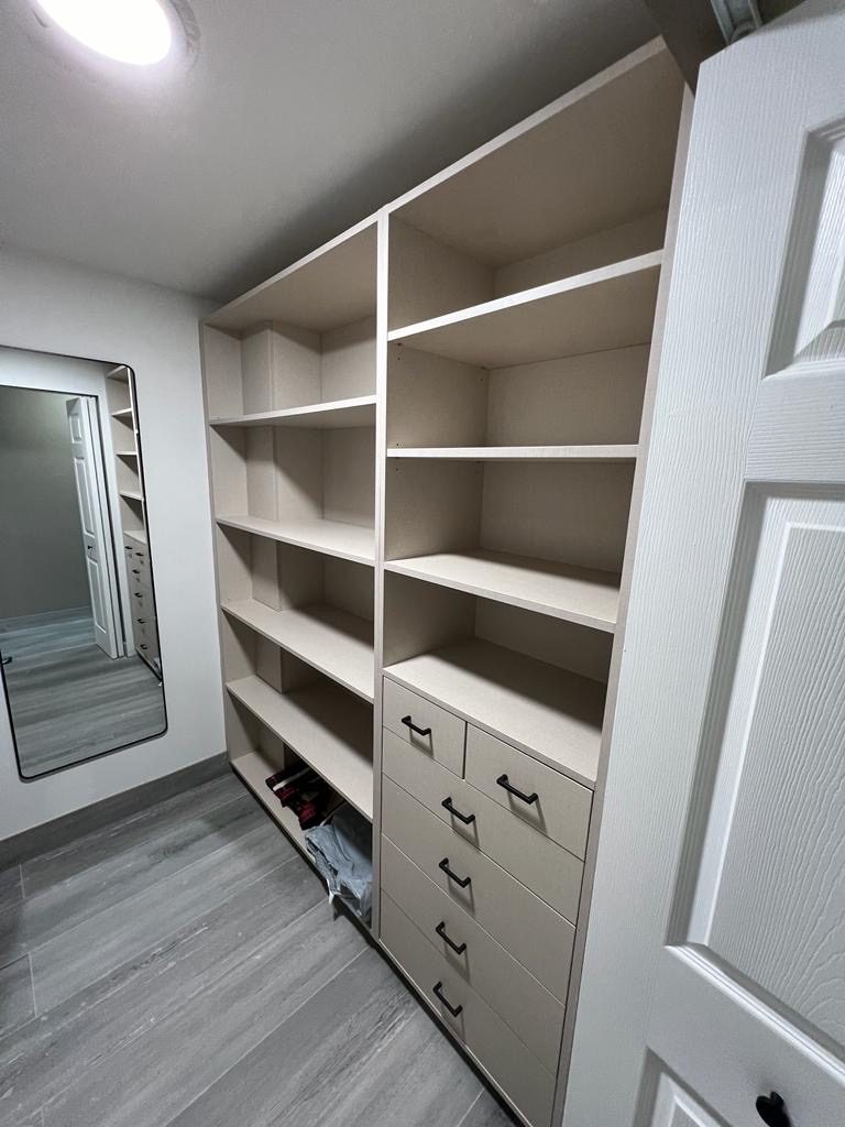 A clean modern walk-in closet with beige shelves, drawers and grey flooring.