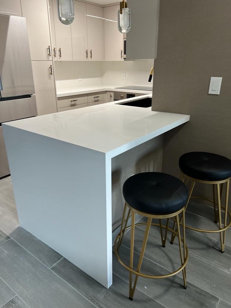 A modern kitchen with a white waterfall island and two black bar stools.