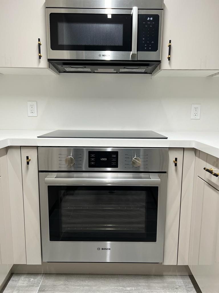 A modern kitchen with a built-in stainless steel oven and microwave and light cabinets.