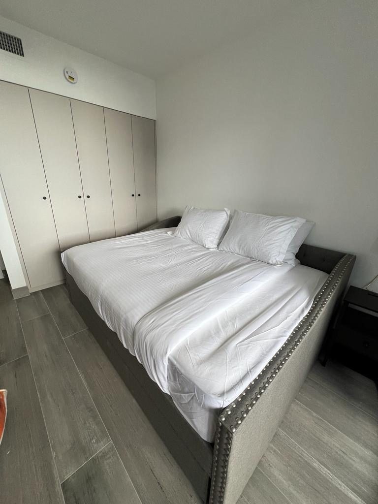 A bedroom with a grey bed and white bedding beside light coloured floor to ceiling closets.