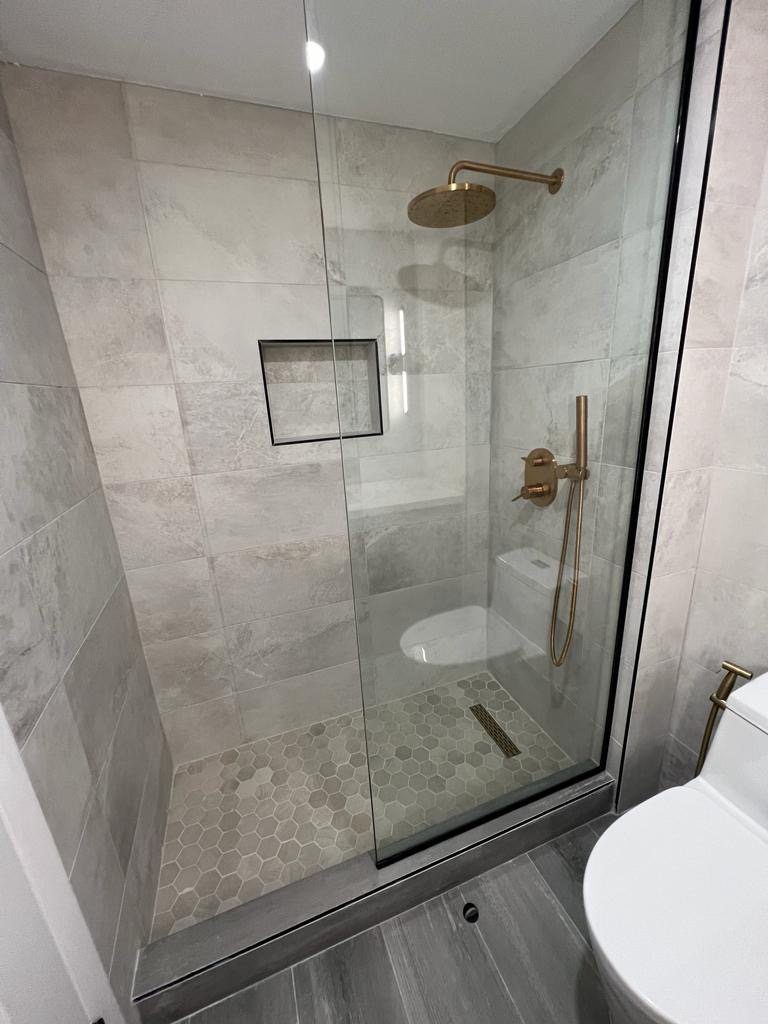 A walk-in shower with grey tiles and modern gold plumbing fixtures.