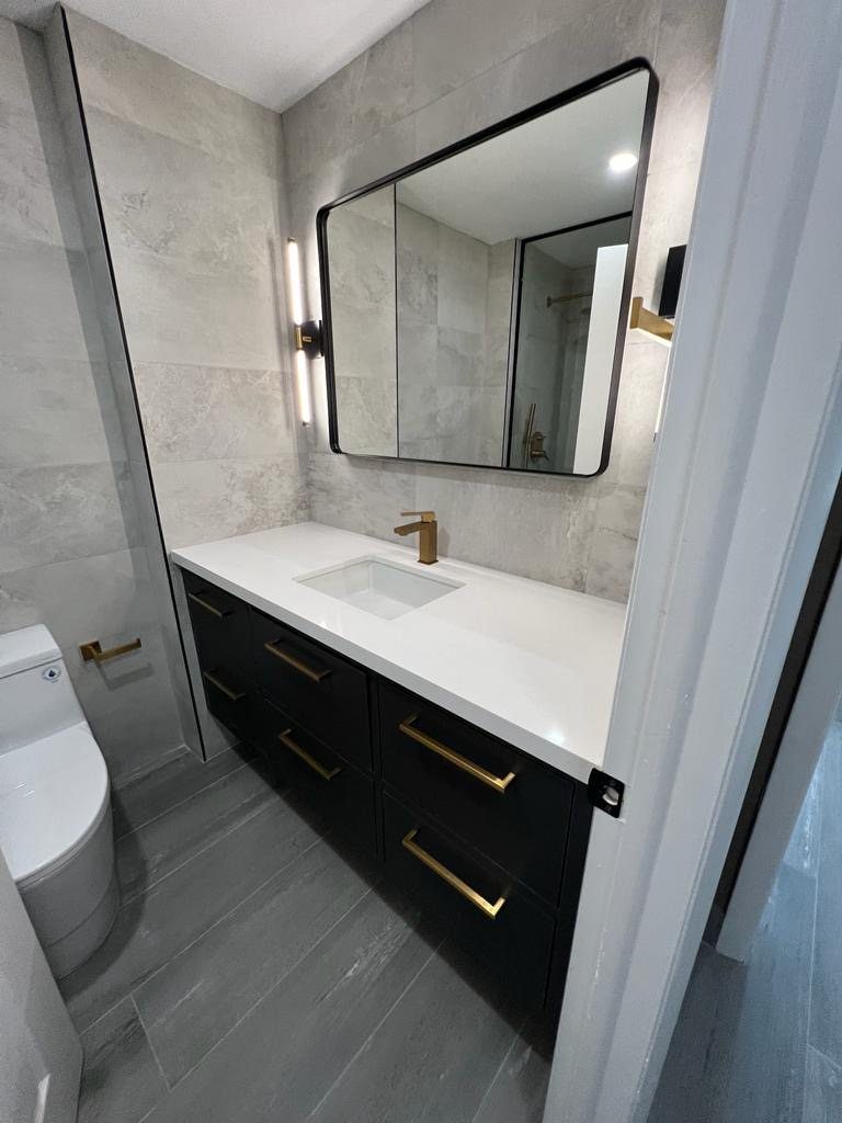 A modern bathroom vanity with black cabinets, gold hardware and stone tiled walls.